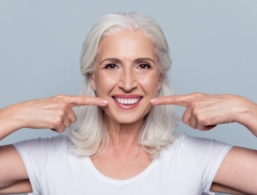 Woman pointing to flawless smile after partial denture treatment